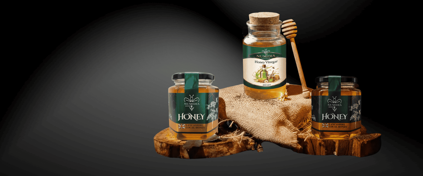 Numidia Honey jars displayed on wooden pieces with a honey dipper against a dark background, showcasing premium British honey.