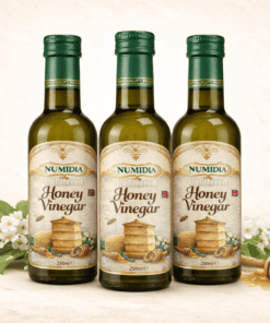 Three bottles of Numidia 250ml Unfiltered Honey Vinegar displayed together on a cream background with flowers, honey dipper, and honeycomb.